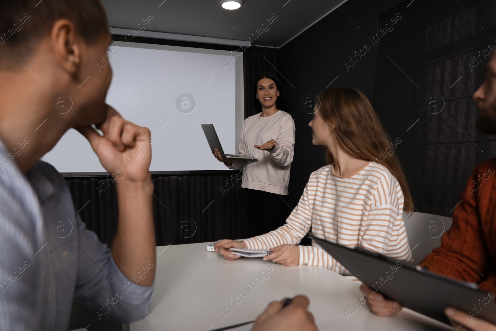 Photo of Business people listening to speaker in conference room with video projection screen