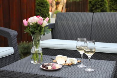 Vase with roses, glasses of wine and food on rattan table on outdoor terrace