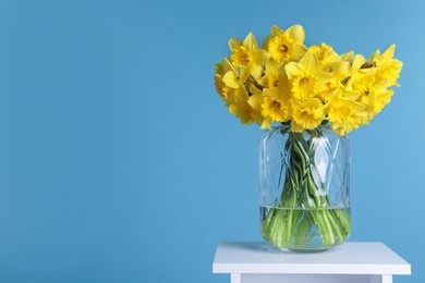 Beautiful daffodils in vase on white table against light blue background, space for text