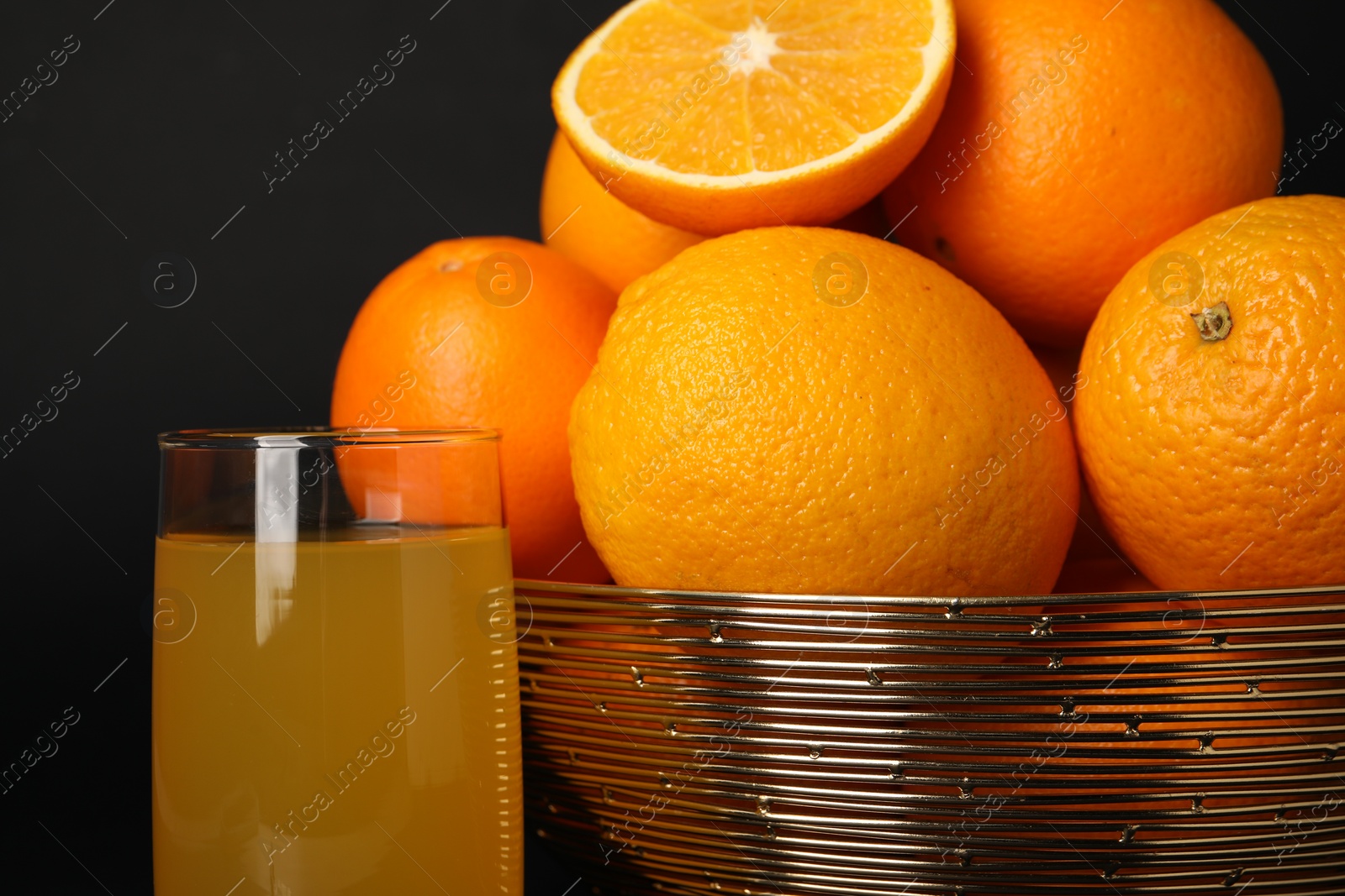 Photo of Bowl with ripe oranges and fresh juice on black background, closeup