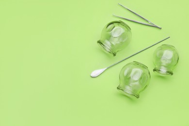 Photo of Glass cups, tweezers and torch on light green background, flat lay with space for text. Cupping therapy