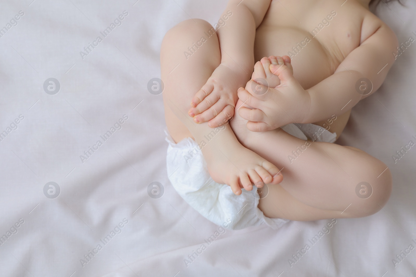 Photo of Little baby in diaper lying on bed, top view