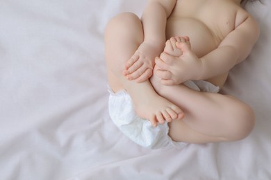 Photo of Little baby in diaper lying on bed, top view