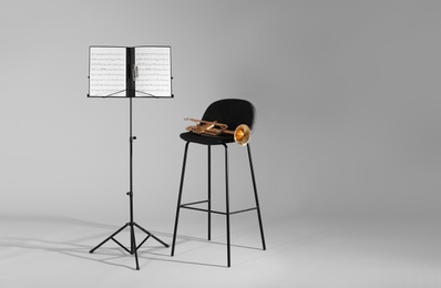 Photo of Trumpet, chair and note stand with music sheets on grey background. Space for text