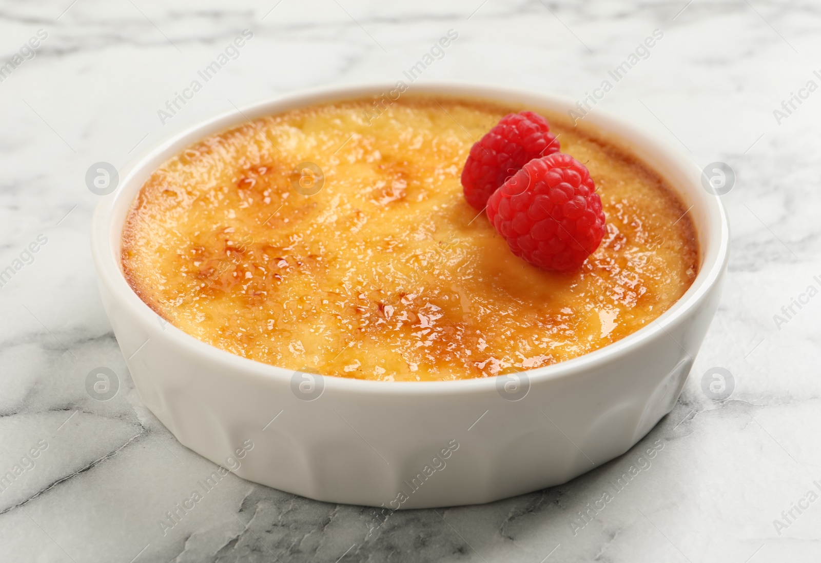 Photo of Delicious creme brulee with raspberries on white marble table, closeup view