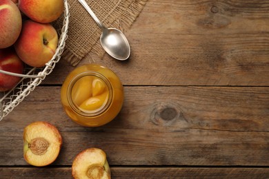 Photo of Canned peach halves in glass jar on wooden table, flat lay. Space for text