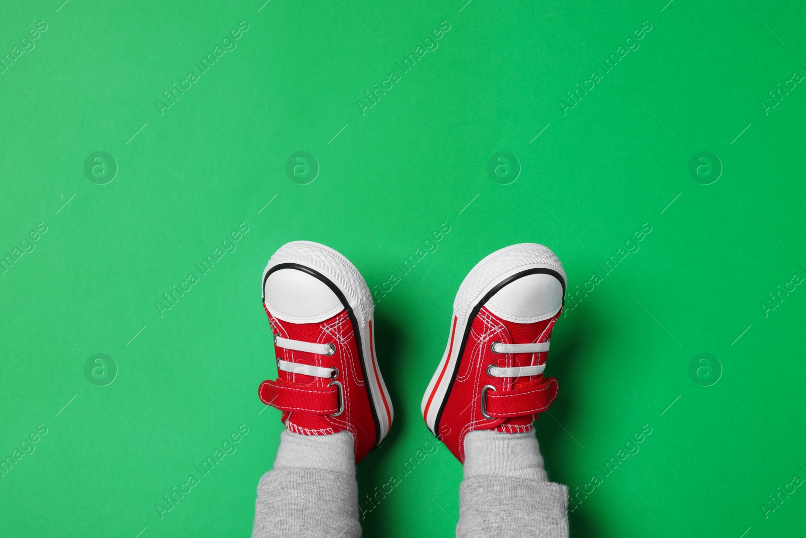 Photo of Little child in stylish red gumshoes on green background, top view