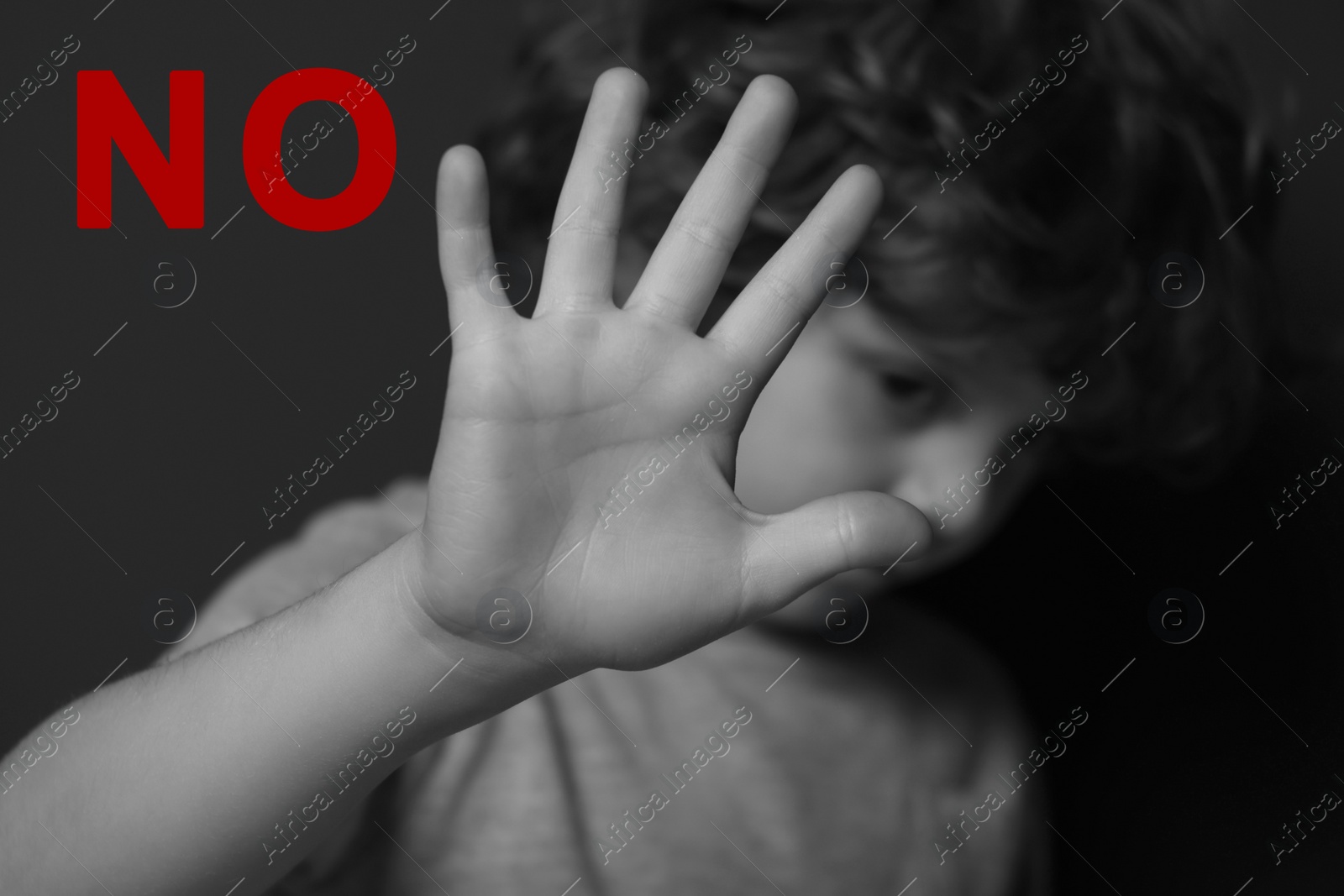 Image of No child abuse. Boy making stop gesture near dark wall, selective focus. Black and white effect