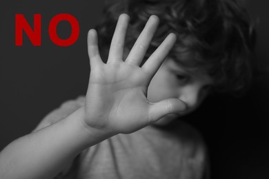 Image of No child abuse. Boy making stop gesture near dark wall, selective focus. Black and white effect