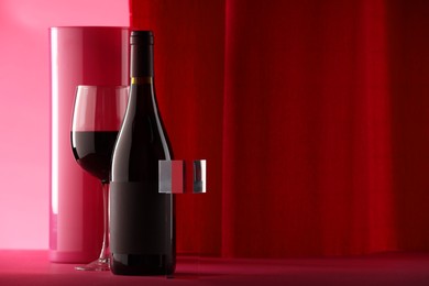 Photo of Stylish presentation of delicious red wine in bottle and glass on color background. Space for text