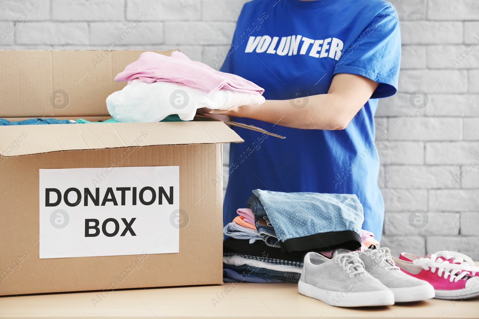 Photo of Female volunteer collecting clothes and shoes into donation box indoors