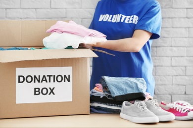 Female volunteer collecting clothes and shoes into donation box indoors