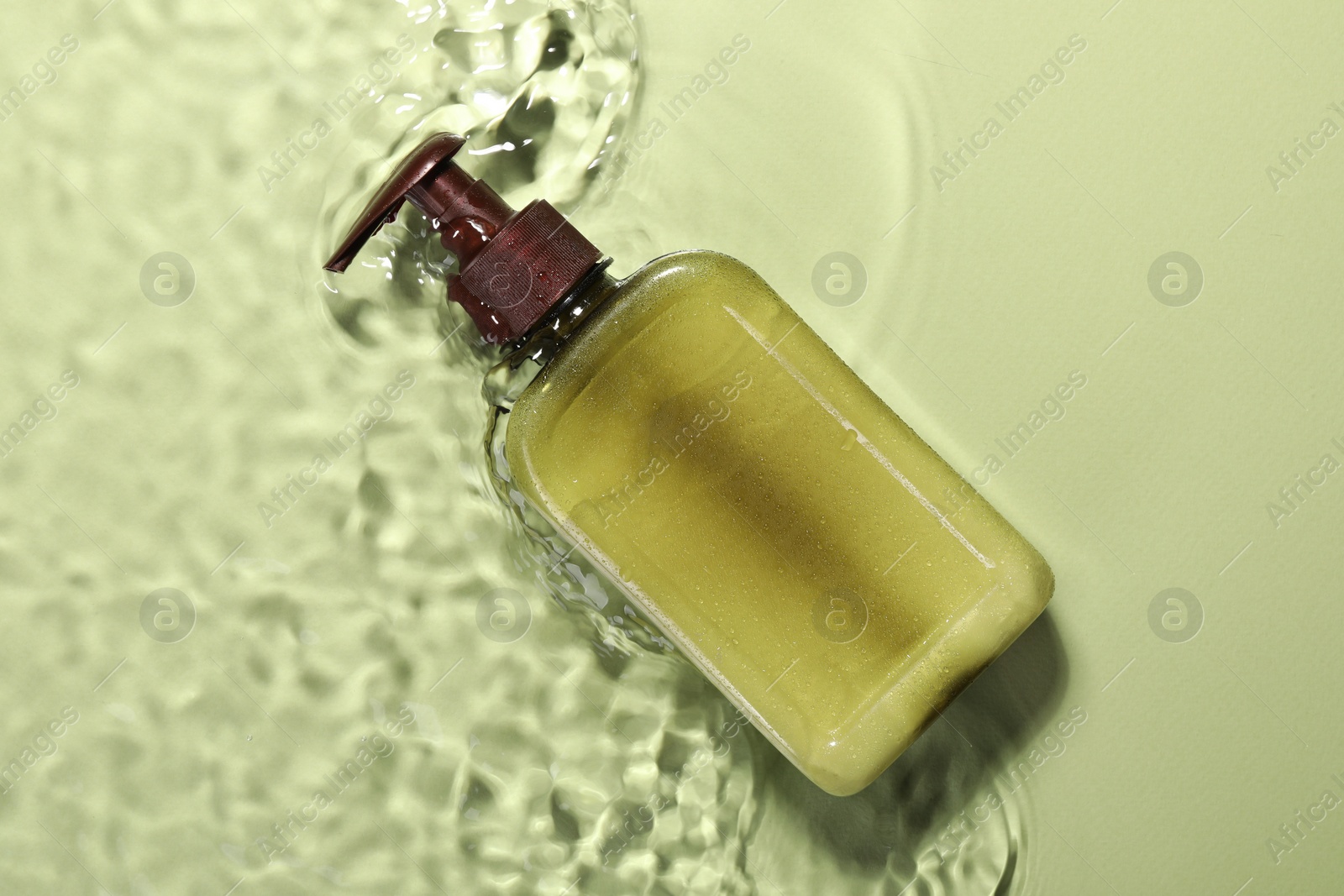 Photo of Bottle of facial cleanser in water against olive background, top view