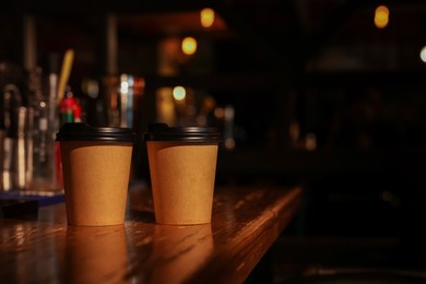 Photo of Paper coffee cups on wooden table in cafe. Space for text