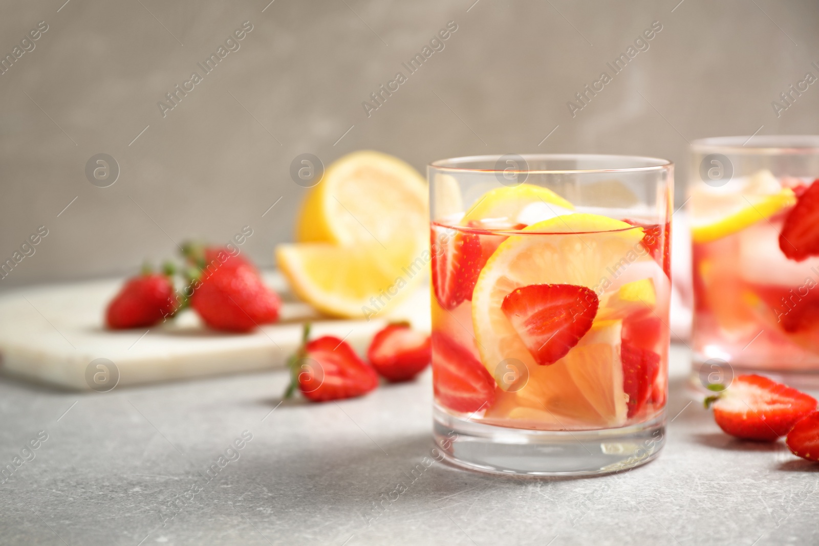 Photo of Tasty refreshing drink with strawberries and lemon on light grey table. Space for text