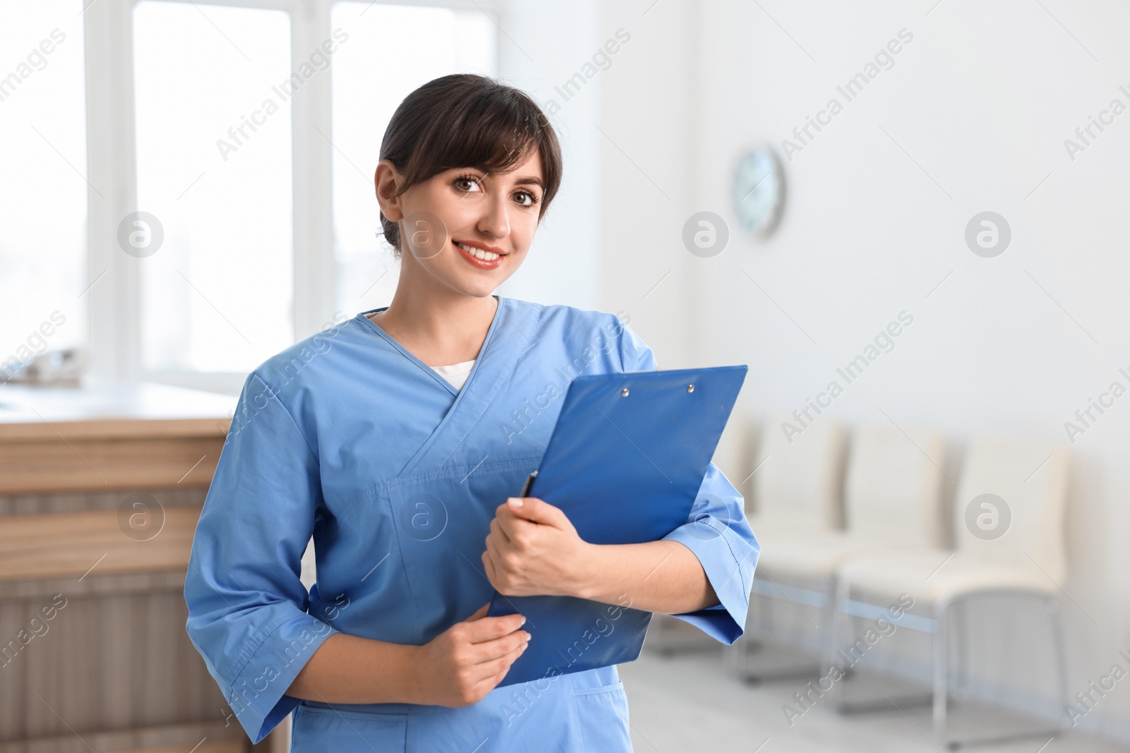 Photo of Portrait of smiling medical assistant with clipboard in hospital. Space for text