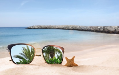 Palms mirroring in sunglasses on sandy beach with starfish near sea