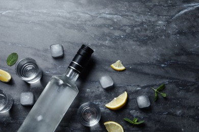Photo of Bottle of vodka, shot glasses, lemon, mint and ice on black marble table, flat lay. Space for text