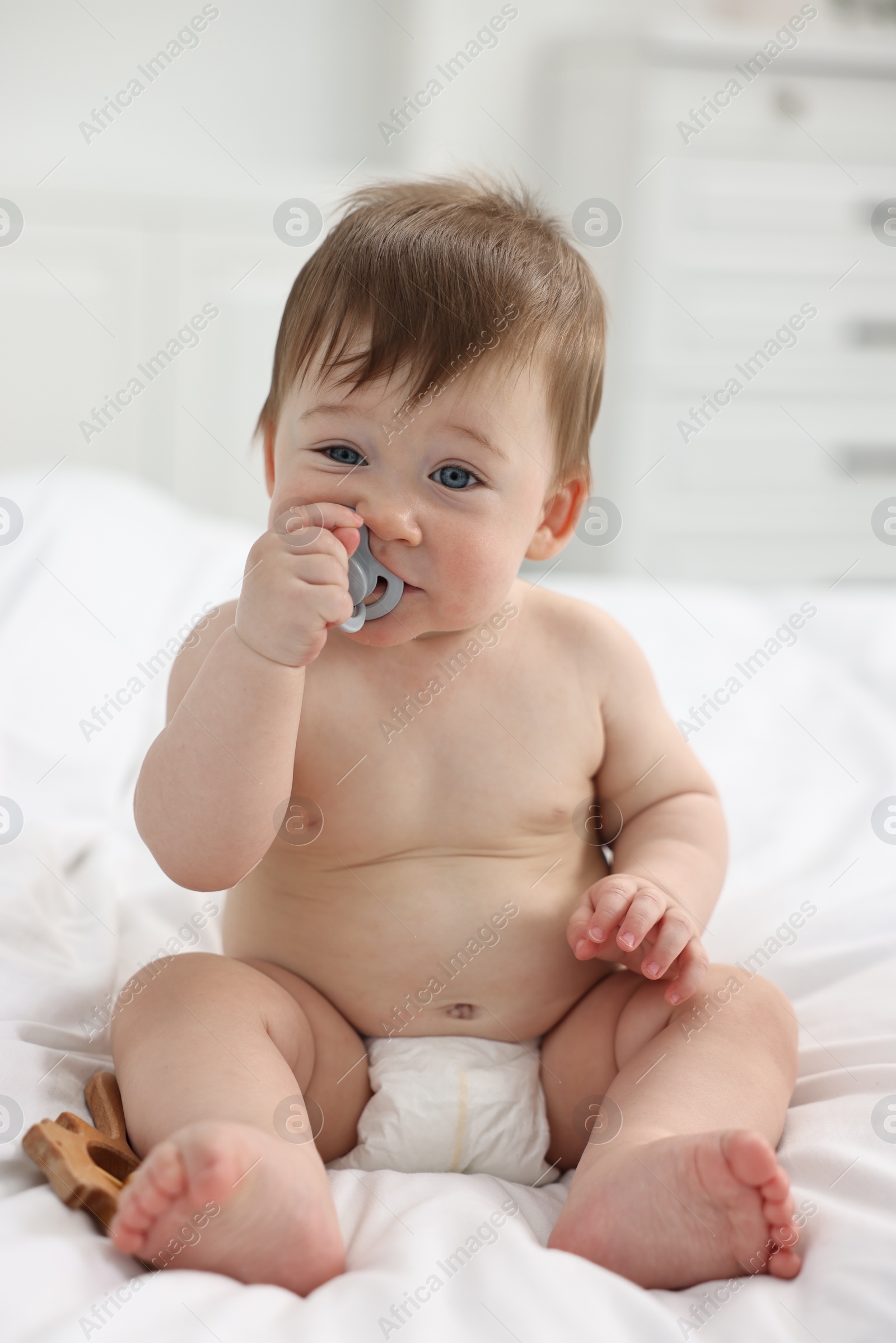 Photo of Cute baby boy with pacifier and wooden rattle on bed at home