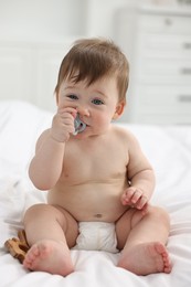 Cute baby boy with pacifier and wooden rattle on bed at home