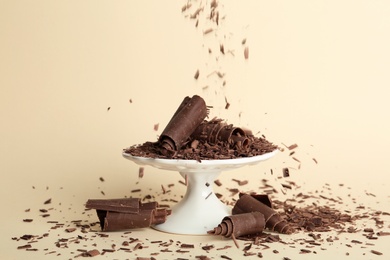 Photo of Sprinkling chocolate curls onto dessert stand on color background