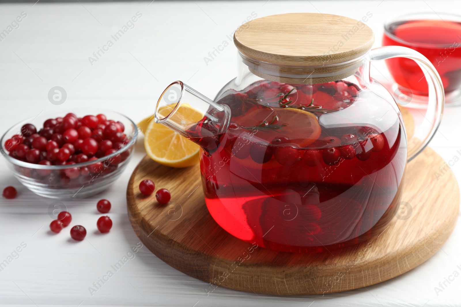 Photo of Tasty hot cranberry tea in teapot, lemon and fresh berries on white wooden table