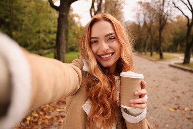 Photo of Portrait of happy woman with paper cup taking selfie in autumn park