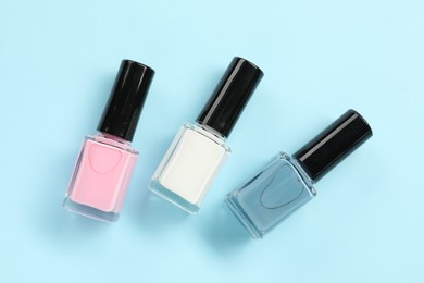 Photo of Bright nail polishes in bottles on light blue background, flat lay