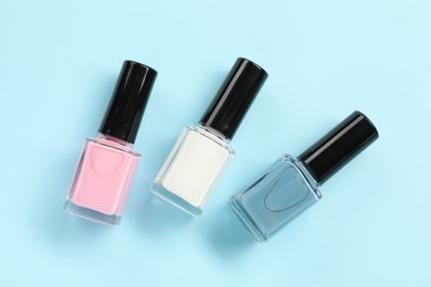 Bright nail polishes in bottles on light blue background, flat lay