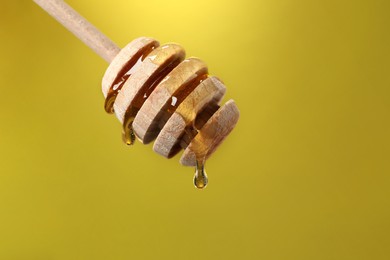 Photo of Delicious honey flowing down from dipper against golden background, closeup. Space for text