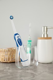 Photo of Electric toothbrushes in glass and toiletries on light grey marble table