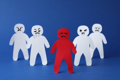 Photo of White paper figures and one red on blue background. Bullying concept