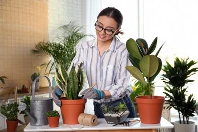 Photo of Young woman taking care of potted plants at home