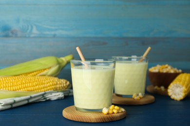 Photo of Tasty fresh corn milk in glasses and cobs on blue wooden table