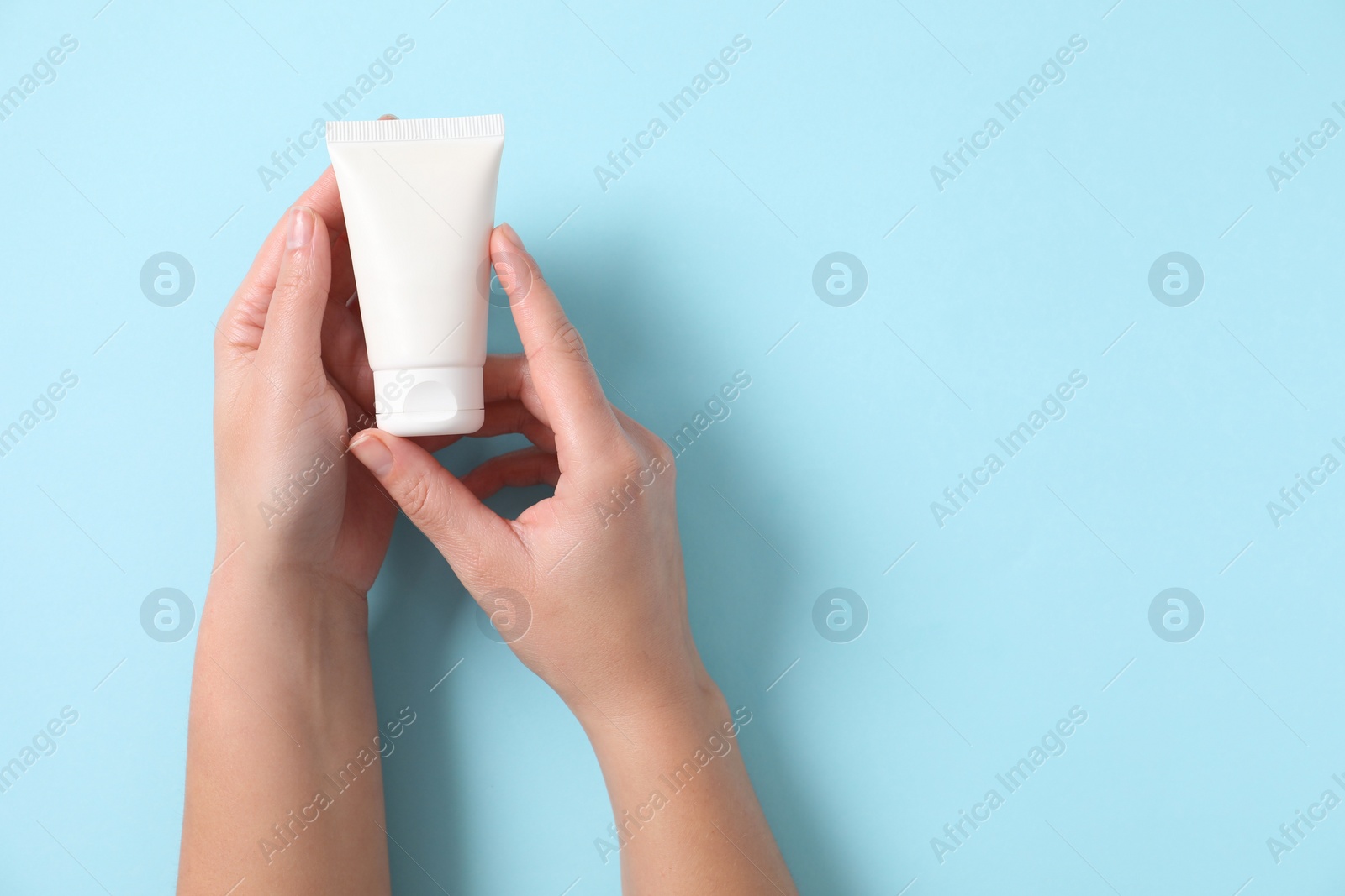 Photo of Woman with tube of hand cream on light blue background, top view. Space for text