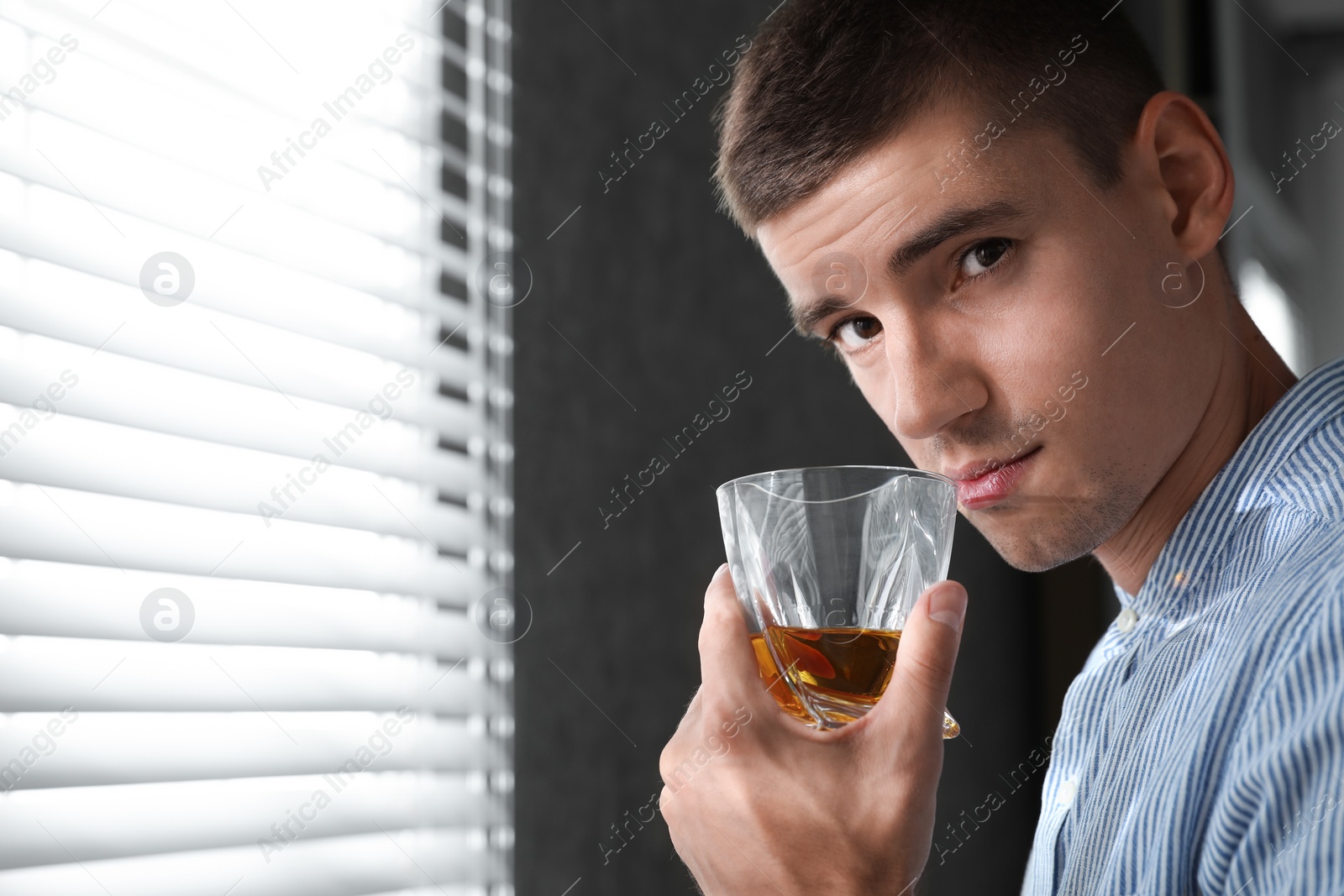 Photo of Young man with glass of whiskey near window indoors. Space for text