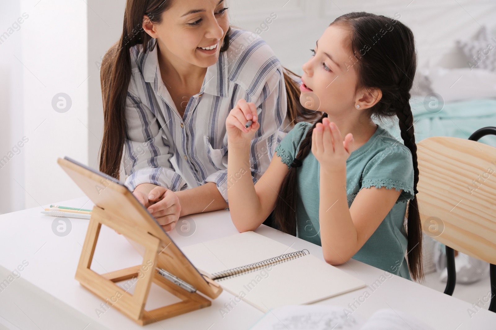 Photo of Mother helping her daughter doing homework with tablet at home