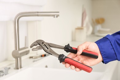 Photo of Plumber with spanner near sink in kitchen, closeup. Water tap installation
