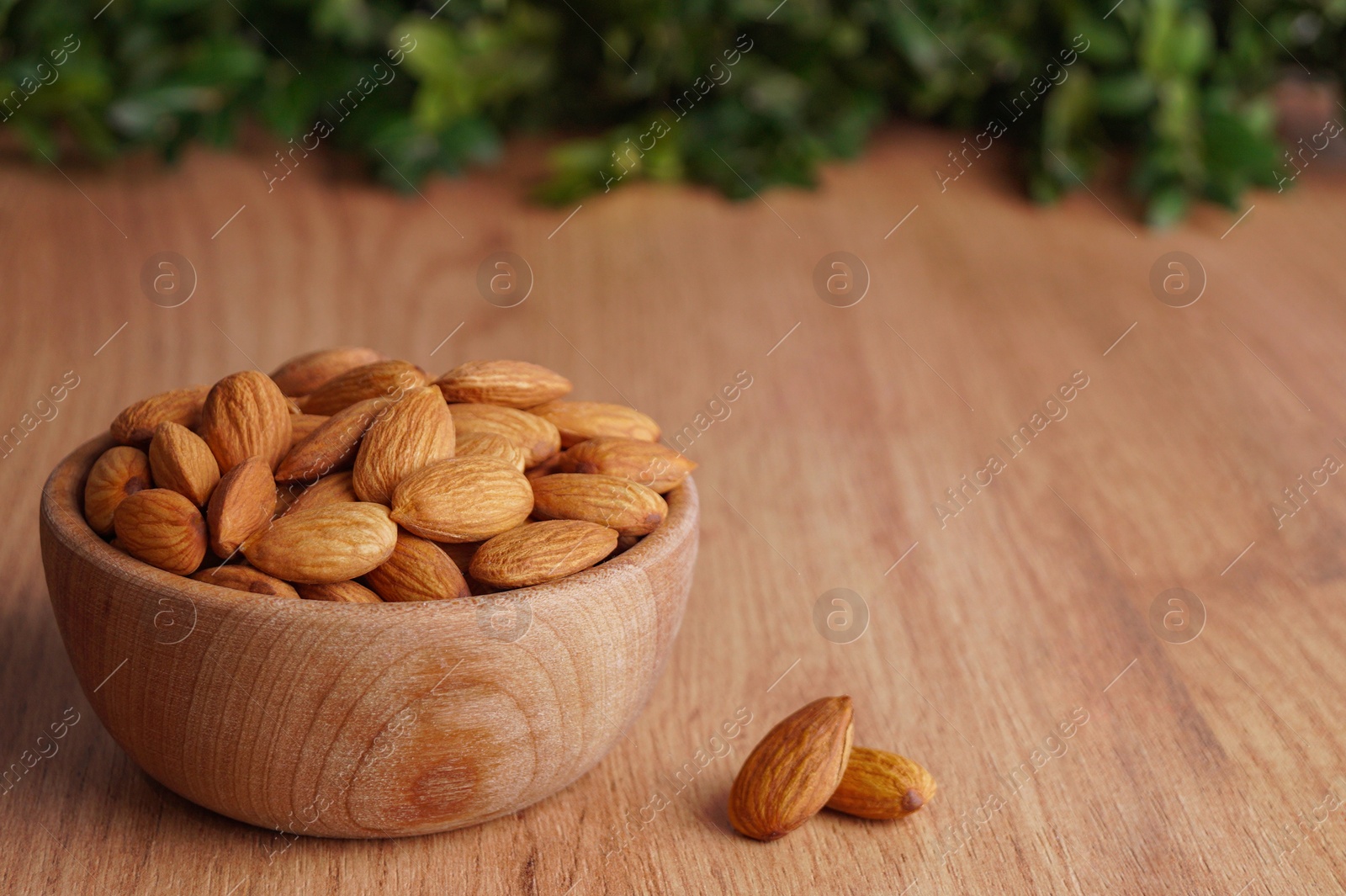 Photo of Tasty almonds in bowl on wooden table, space for text