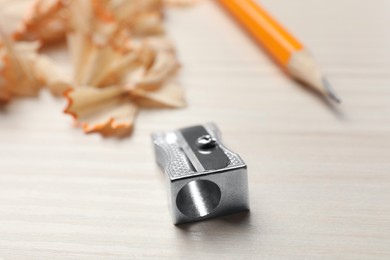 Metal sharpener near pencil and shavings on white wooden table, closeup