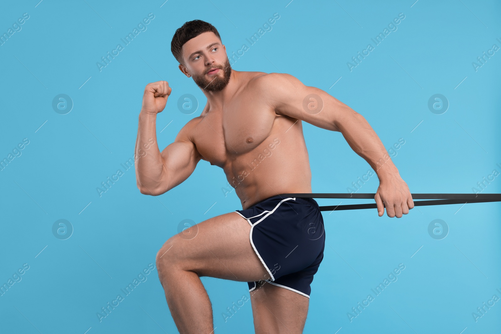 Photo of Young man exercising with elastic resistance band on light blue background