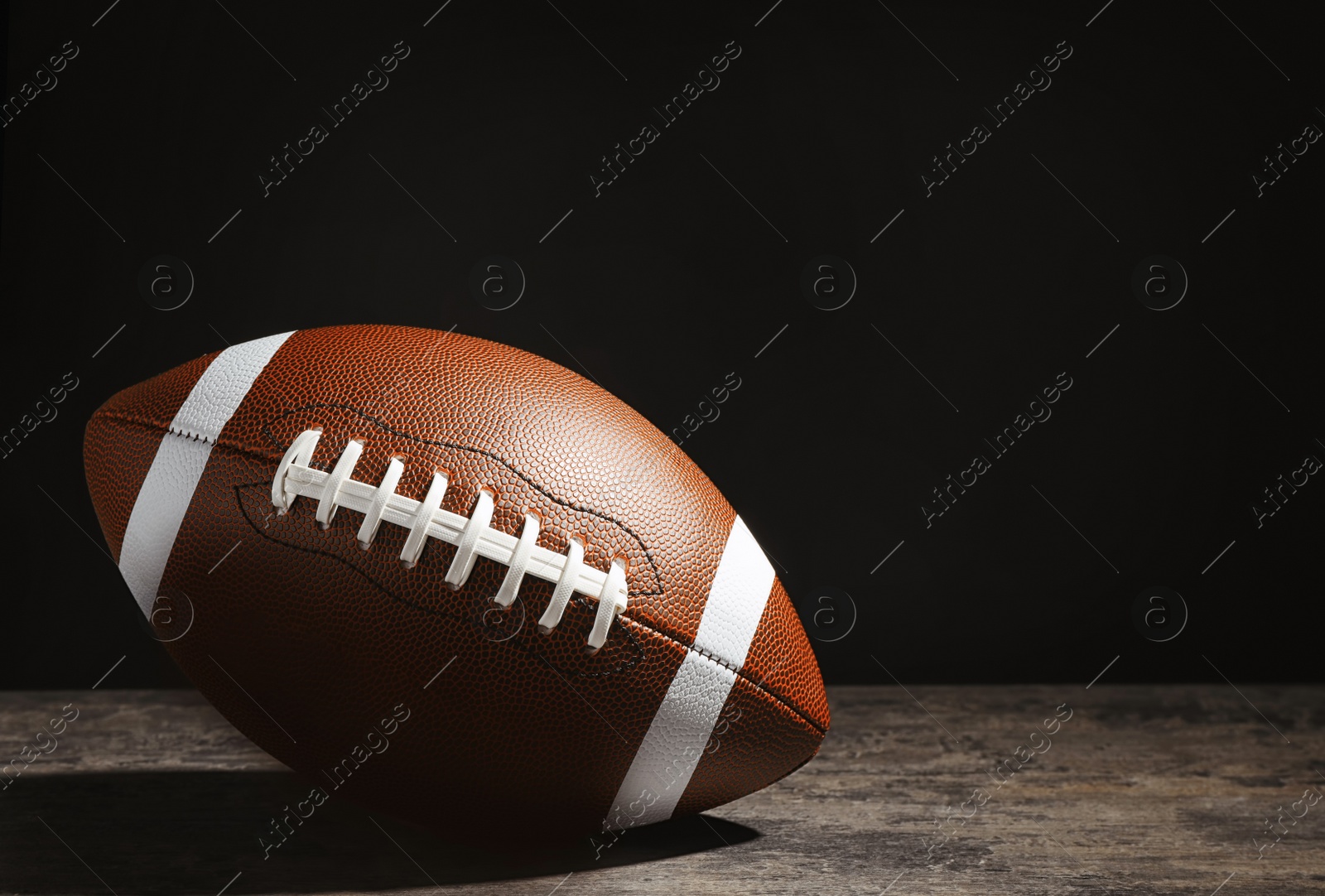 Photo of New American football ball on table against dark background