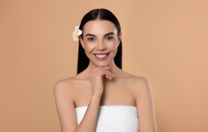 Photo of Young woman with plumeria flower in hair on beige background. Spa treatment