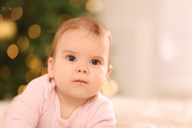 Portrait of cute little baby against blurred festive lights, space for text. Winter holiday