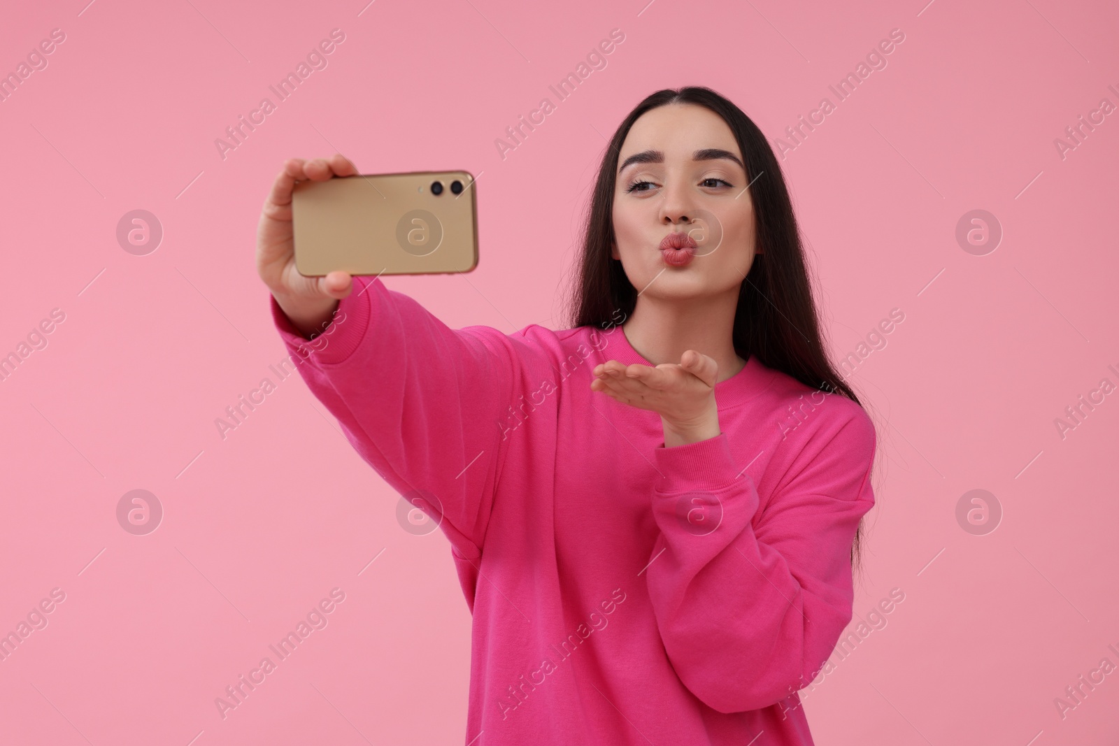Photo of Young woman taking selfie with smartphone and blowing kiss on pink background