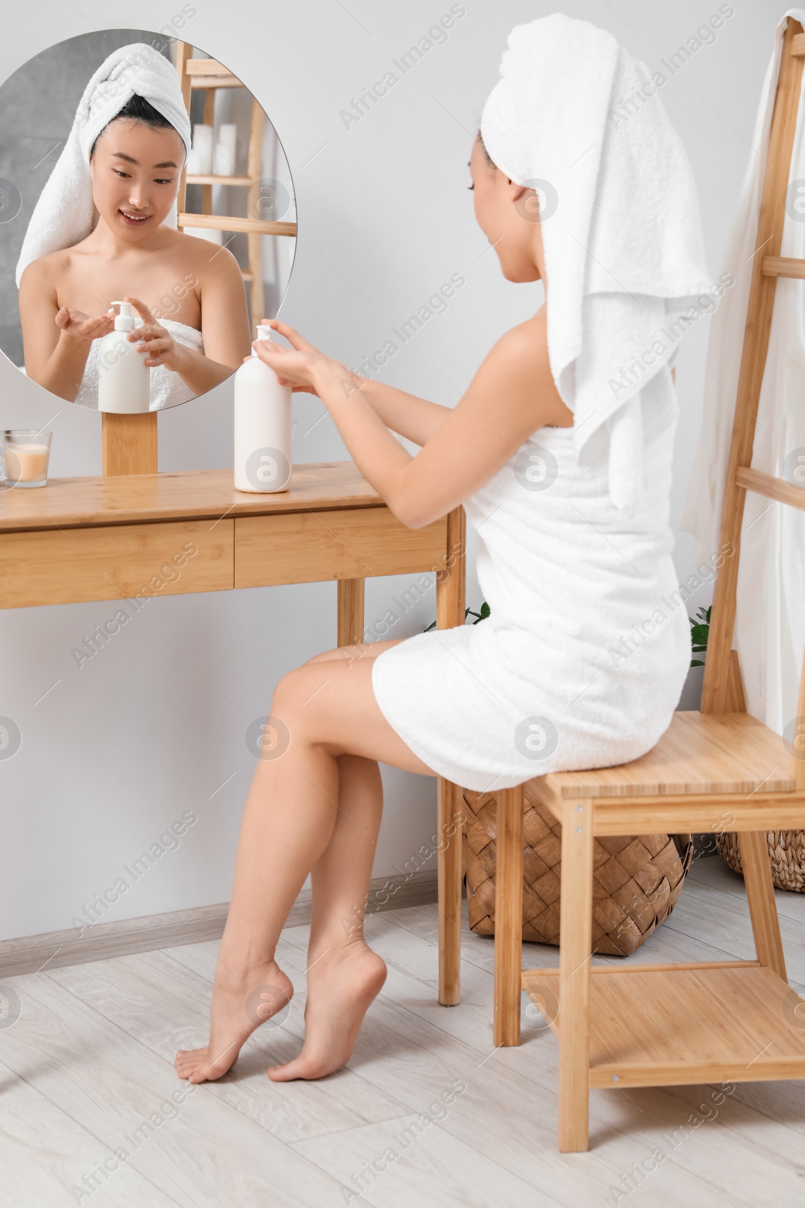 Photo of Beautiful young Asian woman applying body cream on hands in bathroom