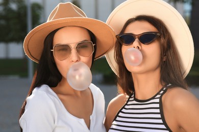 Beautiful women in stylish sunglasses blowing gums outdoors on sunny day