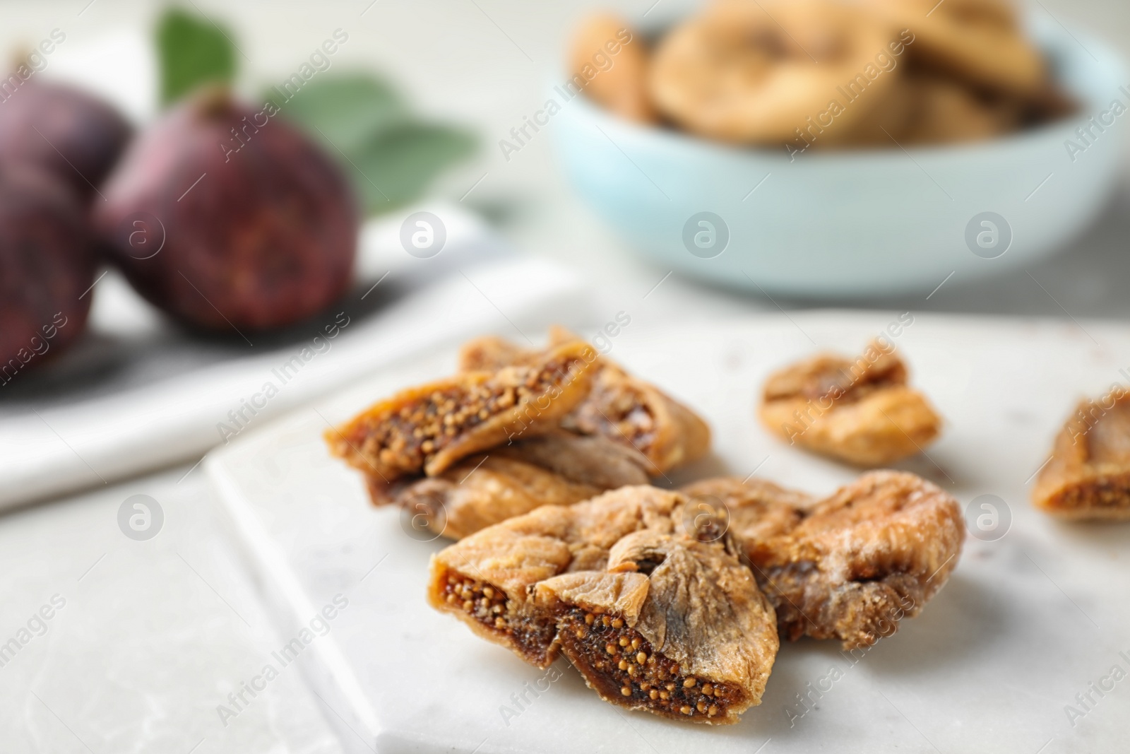 Photo of Marble board with cut dried figs on light table, closeup. Space for text