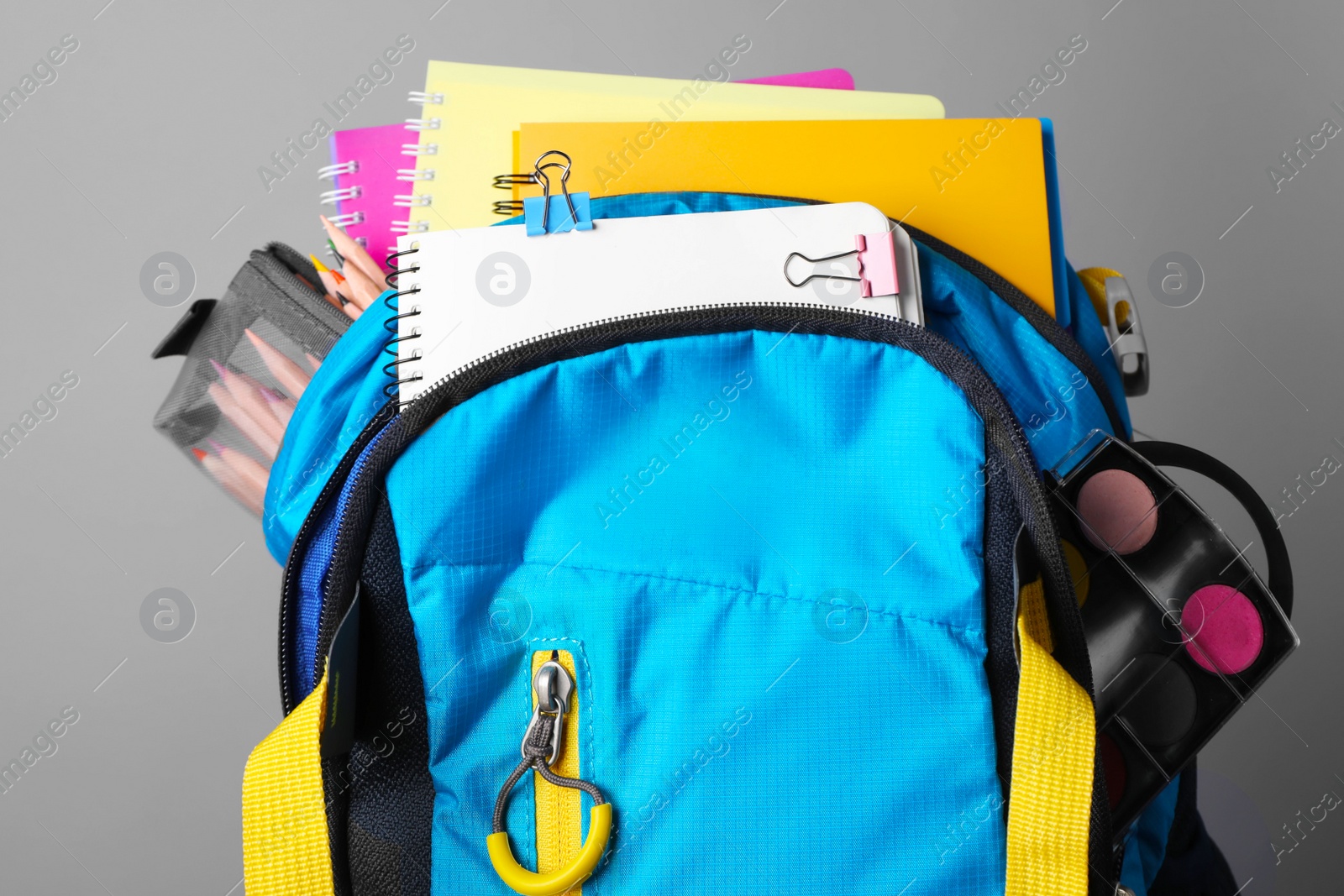 Photo of Children's backpack with different school stationery on grey background, closeup