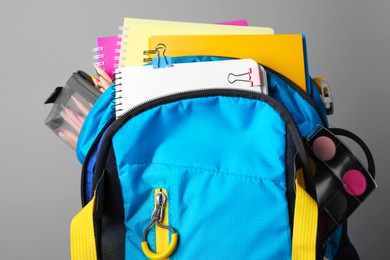 Photo of Children's backpack with different school stationery on grey background, closeup